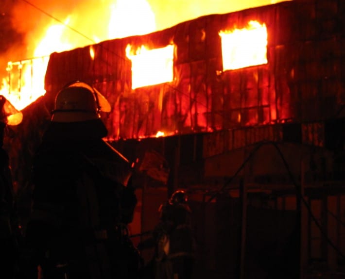 Voluntario frente a una estructura en llamas durante un incendio nocturno