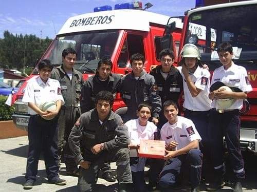 Cadetes con uniforme de trabajo y cascos junto a dos carros bomba