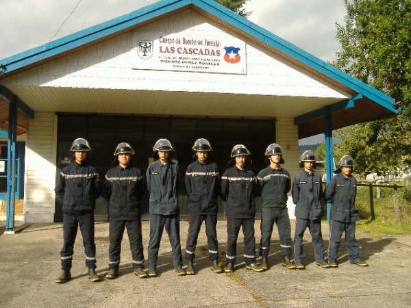 Nueve cadetes en fila, con casco y tenida de trabajo, frente al cuartel de bomberos forestales Las Cascadas