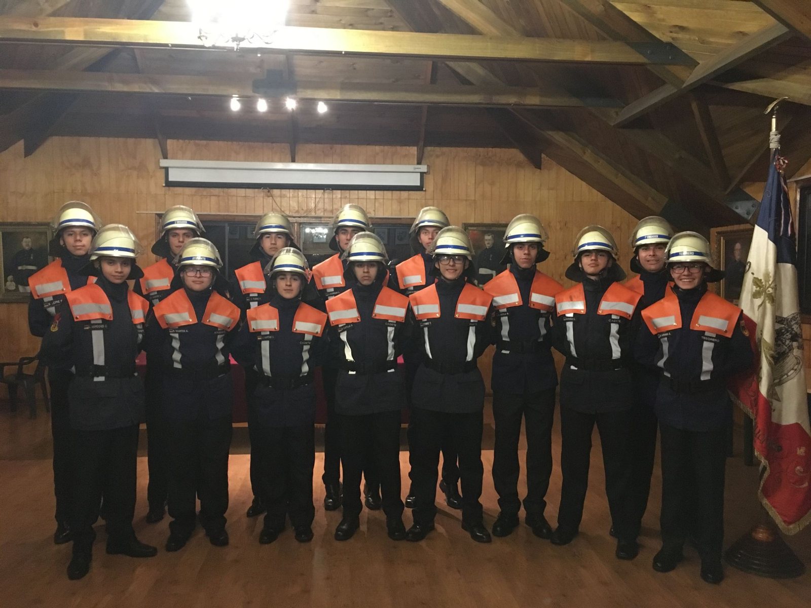 Cadetes de la Brigada con casco blanco y esclavina naranja en la sala de sesiones, junto al estandarte