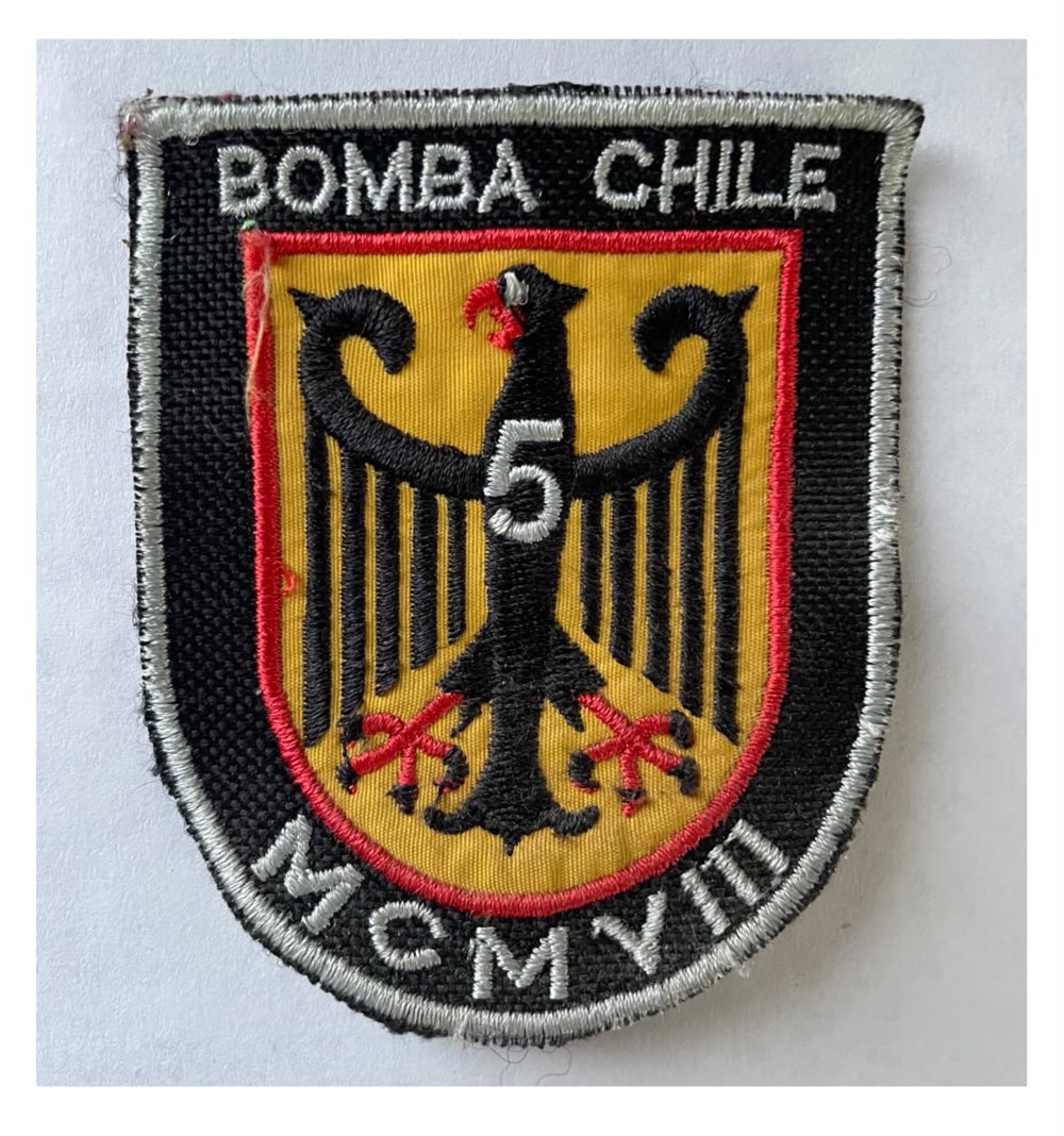 Parche bordado original del centenario: Bomba Chile y MCMVIII en hilo plateado sobre negro, con el águila negra y el 5 sobre fondo amarillo